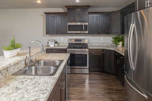 Kitchen featuring stainless steel appliances, sink, light stone counters, dark hardwood / wood-style floors, and dark brown cabinetry