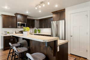 Kitchen featuring a center island with sink, appliances with stainless steel finishes, dark wood-type flooring, and a breakfast bar