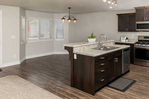 Kitchen featuring dark hardwood / wood-style floors, appliances with stainless steel finishes, sink, decorative light fixtures, and a center island with sink