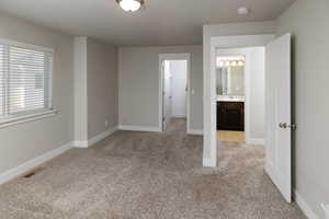 Unfurnished bedroom featuring ensuite bath, sink, and light carpet