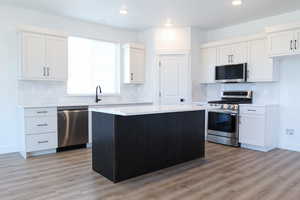 Kitchen with white cabinets, a center island, appliances with stainless steel finishes, and light wood-type flooring