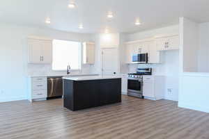 Kitchen with white cabinets, a kitchen island, appliances with stainless steel finishes, light wood-type flooring, and decorative backsplash