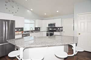 Kitchen with a breakfast bar, light stone counters, appliances with stainless steel finishes, and white cabinetry