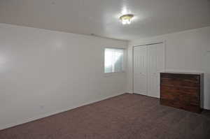 Unfurnished bedroom featuring a textured ceiling, dark colored carpet, and a closet