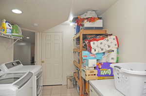 Clothes washing area with light tile patterned floors, a textured ceiling, and washing machine and dryer