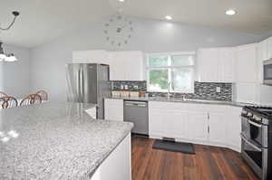 Kitchen with dark hardwood / wood-style flooring, stainless steel appliances, sink, white cabinetry, and light stone counters