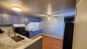 Kitchen with sink, black appliances, light wood-type flooring, a textured ceiling, and ceiling fan