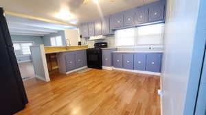 Kitchen featuring gas stove, beam ceiling, blue cabinets, and light hardwood / wood-style floors