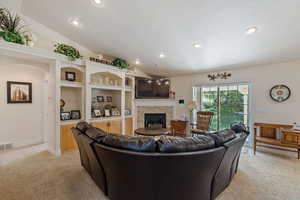 Carpeted living room featuring built in features, a stone fireplace, and vaulted ceiling