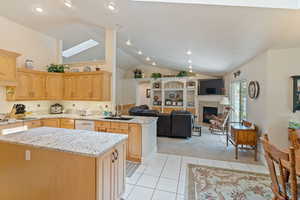 Kitchen with white dishwasher, sink, light tile patterned floors, a kitchen island, and a skylight