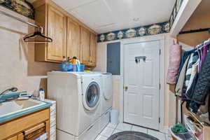 Laundry room with light tile patterned floors, electric panel, washing machine and clothes dryer, cabinets, and sink