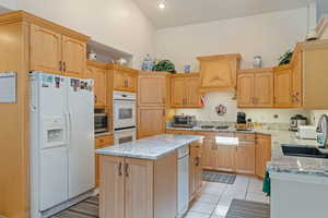 Kitchen with custom exhaust hood, white appliances, light stone countertops, a kitchen island, and light tile patterned floors