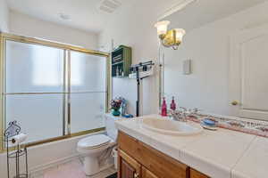 Full bathroom featuring combined bath / shower with glass door, vanity, tile patterned flooring, and toilet