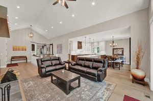 Living room featuring light hardwood / wood-style floors, ceiling fan with notable chandelier, and high vaulted ceiling