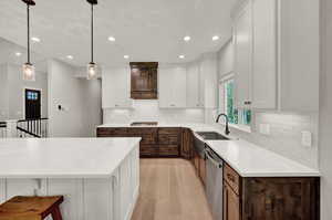 Kitchen featuring stainless steel appliances, light hardwood / wood-style floors, decorative light fixtures, decorative backsplash, and white cabinetry