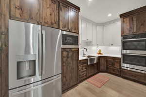 Kitchen with dark brown cabinets, light wood-type flooring, sink, appliances with stainless steel finishes, and backsplash