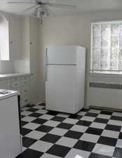 Kitchen featuring radiator heating unit, tile patterned flooring, ceiling fan, and white appliances