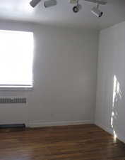 Empty room with dark hardwood / wood-style flooring, radiator, rail lighting, and ceiling fan