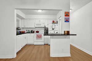 Kitchen featuring white cabinets, light hardwood / wood-style flooring, white appliances, and kitchen peninsula