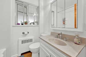 Bathroom featuring vanity, radiator, hardwood / wood-style floors, and toilet