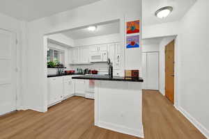 Kitchen featuring white cabinetry, white appliances, light wood-type flooring, and kitchen peninsula