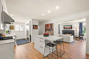 Kitchen featuring light hardwood flooring, white cabinets, wall chimney range hood, light stone counters, and crown molding