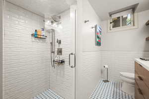 Bathroom featuring vanity, tile walls, toilet, a shower with door, and tile patterned flooring