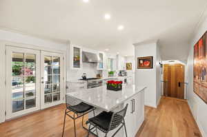 Kitchen featuring light hardwood flooring, wall chimney range hood, white cabinets, a kitchen island, and high end stainless steel range oven