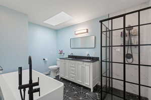 Bathroom featuring a skylight, tile patterned flooring, a bathtub, toilet, and dual vanity