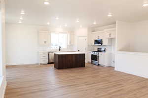 Kitchen with appliances with stainless steel finishes, light wood-type flooring, a center island, and white cabinetry