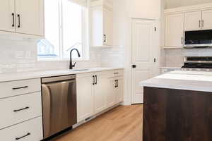 Kitchen with appliances with stainless steel finishes, light wood-type flooring, tasteful backsplash, and white cabinetry