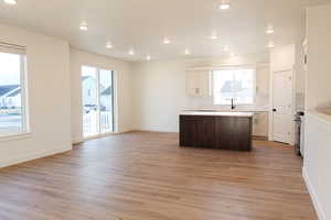 Kitchen with white cabinetry, stainless steel stove, a kitchen island, light hardwood / wood-style flooring, and decorative backsplash