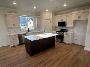 Kitchen with hardwood / wood-style flooring, decorative backsplash, a kitchen island, white cabinetry, and stainless steel appliances