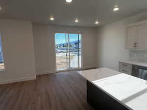 Kitchen featuring hardwood / wood-style flooring, light stone counters, tasteful backsplash, dishwasher, and white cabinetry