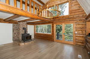 Unfurnished living room featuring a wood stove, wood-type flooring, high vaulted ceiling, and rustic walls