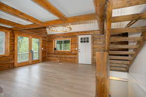 Unfurnished room with a chandelier, beam ceiling, hardwood / wood-style floors, and rustic walls