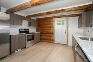 Kitchen featuring appliances with stainless steel finishes, light hardwood / wood-style flooring, tasteful backsplash, and beam ceiling