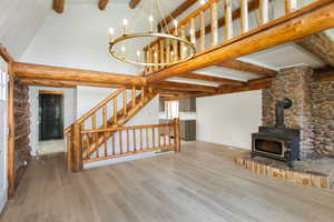 Unfurnished living room with a wood stove, an inviting chandelier, wood-type flooring, and vaulted ceiling with beams