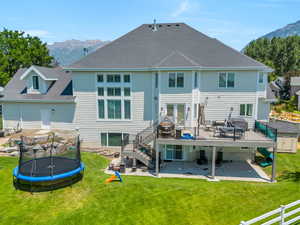 Back of house featuring a patio, a deck with mountain view, a trampoline, and a yard