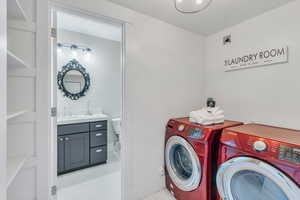 Clothes washing area with light tile patterned flooring, washer and dryer, and sink