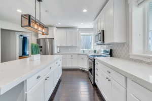 Kitchen featuring hanging light fixtures, premium appliances, white cabinets, and backsplash