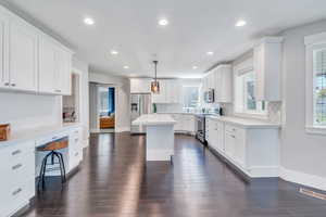 Kitchen with decorative light fixtures, tasteful backsplash, stainless steel appliances, a kitchen island, and dark wood-type flooring