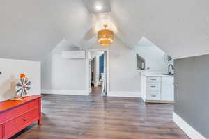 Additional living space featuring sink, a textured ceiling, lofted ceiling, a wall mounted air conditioner, and dark hardwood / wood-style flooring