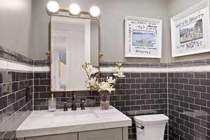 Bathroom featuring tile walls, toilet, vanity, and decorative backsplash