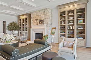 Living area featuring coffered ceiling, beamed ceiling, light hardwood / wood-style flooring, a stone fireplace, and built in shelves