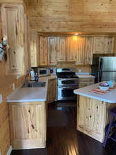 Kitchen with light brown cabinets, wood walls, hardwood / wood-style floors, appliances with stainless steel finishes, and sink