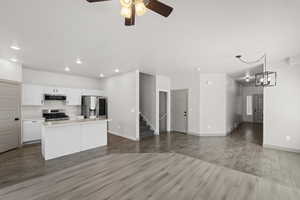 Kitchen with white cabinetry, stainless steel appliances, ceiling fan with notable chandelier, hardwood / wood-style floors, and a center island