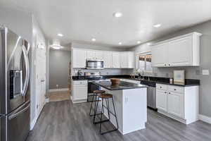Kitchen with hardwood / wood-style flooring, white cabinetry, a kitchen island, and stainless steel appliances