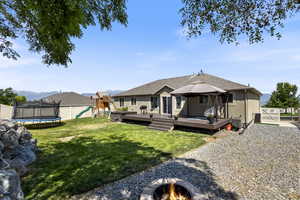 Rear view of property featuring a deck, a hot tub, a lawn, a trampoline, and a playground