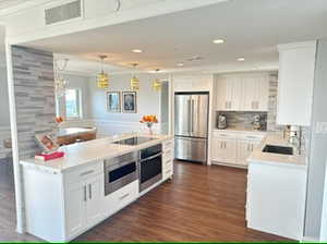 Kitchen featuring decorative light fixtures, stainless steel appliances, dark hardwood / wood-style flooring, white cabinets, and crown molding